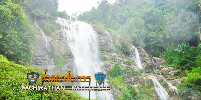 Waterfall with lush green forest and signs indicating Wachirathan Waterfall