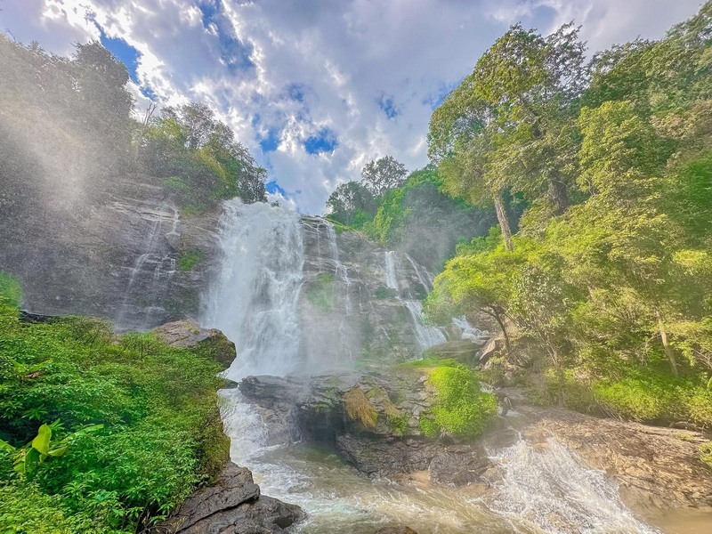 Scenic Waterfall Cascade at Wachirathan Waterfall Waterfall flowing over rocks with trees and a partly cloudy sky in the background at Wachirathan Waterfall.