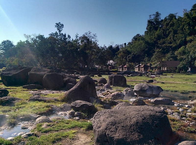 Scenic Natural Landscape at Fang Hot Spring Open grassy landscape with rocks and trees under a clear sky at Fang Hot Spring.
