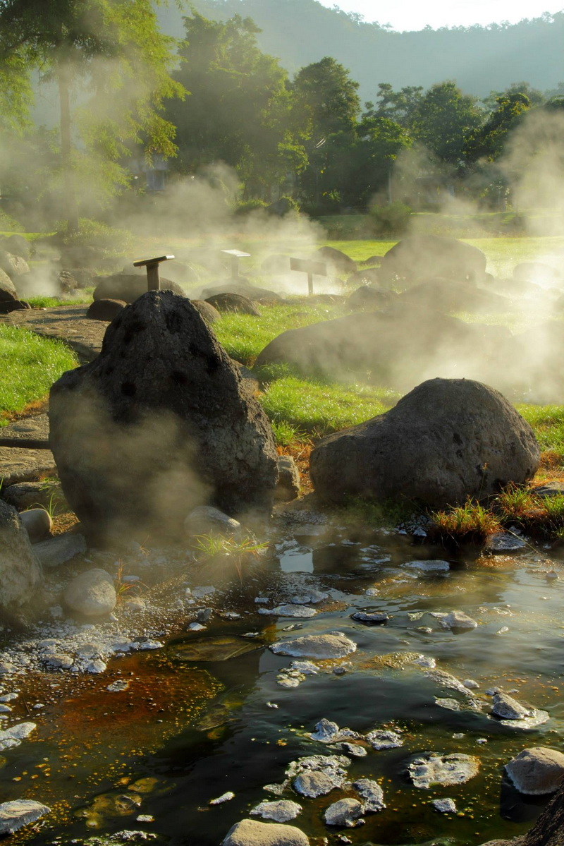 Hot Spring Geothermal Area at Fang Hot Spring Steam rises from hot springs surrounded by rocks and greenery in a geothermal setting at Fang Hot Spring.