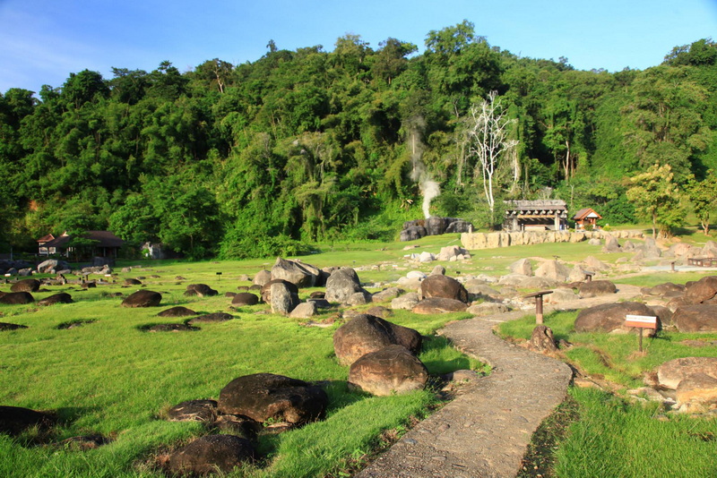 Pathway through grassy area with rocks and hot springs on a green hillside at Fang Hot Springs.