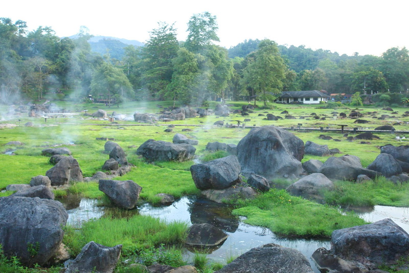 View of steaming hot springs among rocks with trees in the background at Fang Hot Springs.