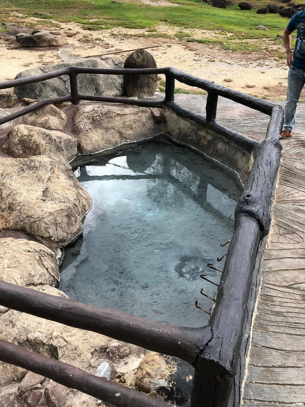 Enclosed outdoor hot spring pool with wooden railing and surrounding rocks at Fang Hot Springs.