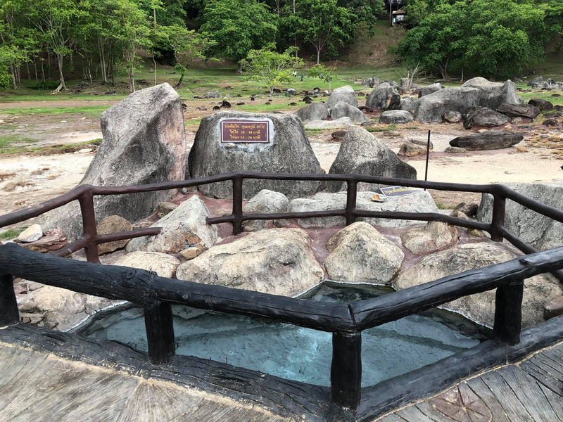 Small hot spring pool with rocks and wooden railing amidst green forest surroundings at Fang Hot Springs.
