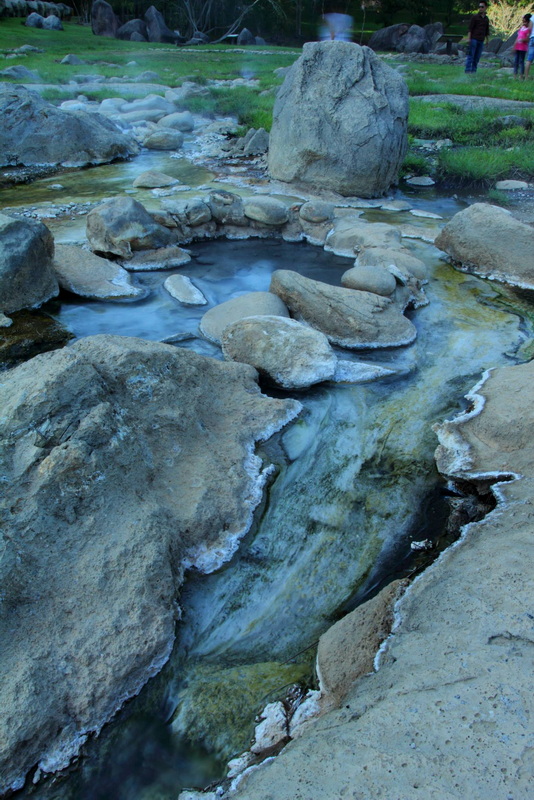 A gentle stream flowing over rocks in a lush park area at Fang Hot Spring.