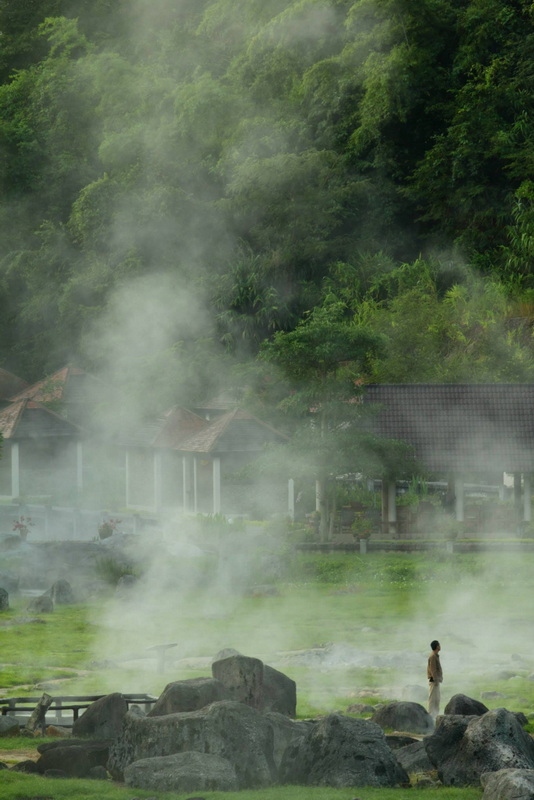 Geothermal Hot Spring Scene at Fang Hot Spring Person standing on rocks near steaming geothermal hot spring in lush forest at Fang Hot Spring.