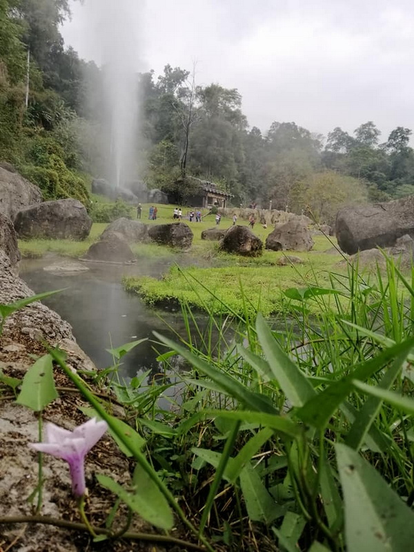 River flowing over rocks with a waterfall and group of people nearby in lush green surroundings at Fang Hot Springs.