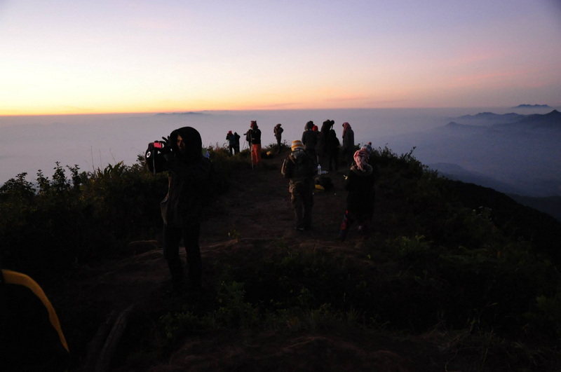 People observing the sunset from a mountain viewpoint with fog and distant mountains at Doi Pha Hom Pok National Park.