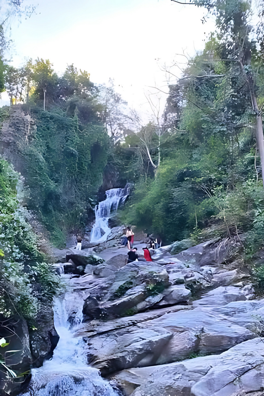 Scenic Waterfall with Visitors at Huai Kaew Waterfall People relaxing on rocks beside a cascading waterfall in a lush green forest at Huai Kaew Waterfall.