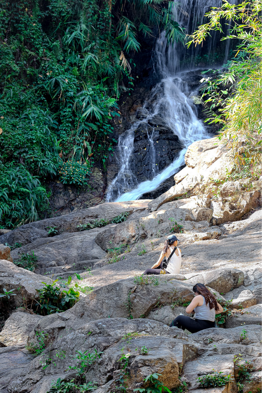 Relaxing by the Waterfall at Huai Kaew Waterfall Two women sit on rocks beside a small waterfall with dense greenery around them at Huai Kaew Waterfall.