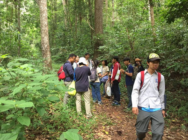 People with backpacks walking along a forest trail enclosed by green trees and plants at Doi Suthep-Pui National Park.