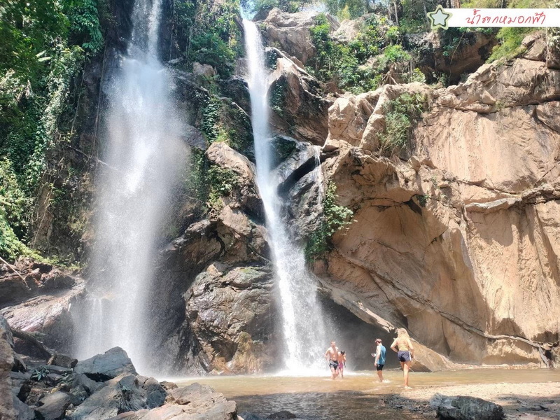 Scenic Waterfall in Jungle at Doi Suthep-Pui National Park People standing at the base of a waterfall surrounded by rocks and lush greenery at Doi Suthep-Pui National Park.