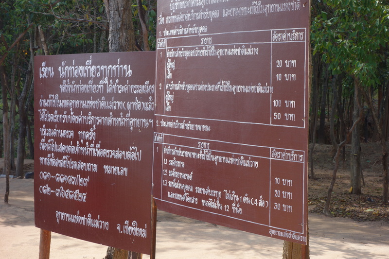 Brown signboard with Thai writing surrounded by trees and lush greenery at Pha Chor.