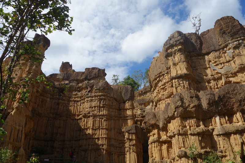 Cliff with layered sedimentary rocks under a partly cloudy sky with greenery around at Pha Chor.