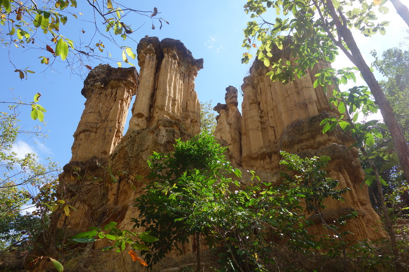 Tall natural rock formations with greenery and a clear blue sky above at Pha Chor.