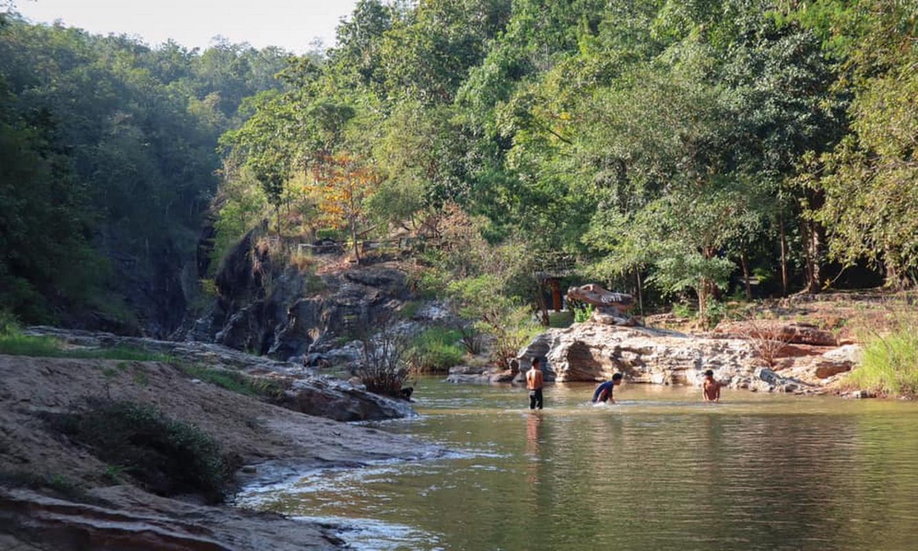 Children enjoying and playing in a forest river with rocks and green foliage at Ob Khan National Park.