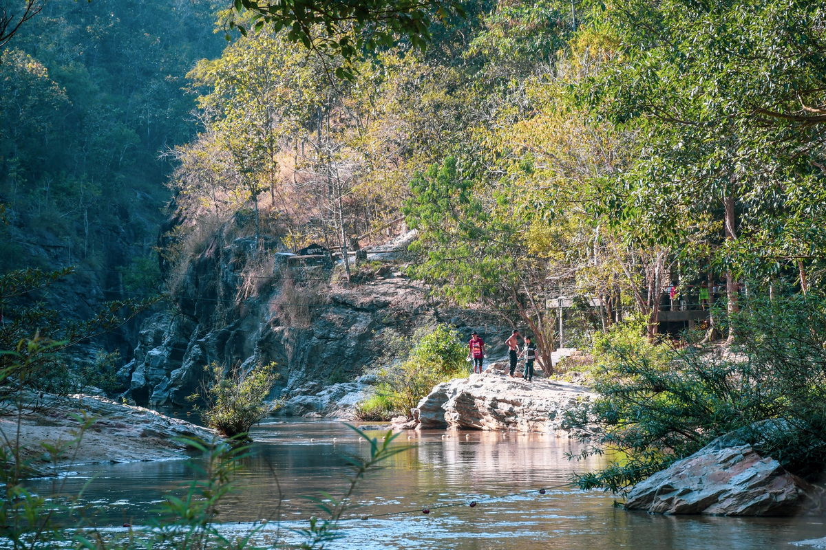 Visitors walking along a rocky riverbank with trees and foliage in a forest at Ob Khan National Park.
