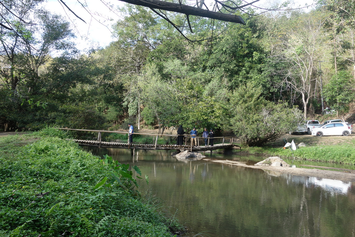 People standing on a small wooden bridge over a stream in a lush forest at Ob Khan National Park.