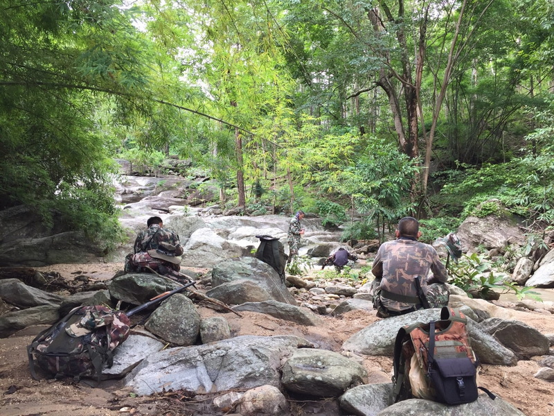 Forest Stream with Camouflage Hikers at Ob Luang National Park People in camouflage resting beside a stream in dense green forest at Ob Luang National Park.