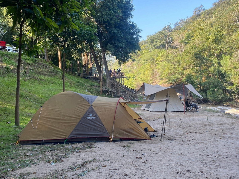 Riverbank Camping Scene at Ob Luang National Park Two tents set up on a sandy riverbank with trees and an observation deck in the background at Ob Luang National Park.