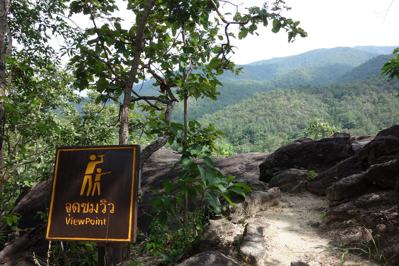 A trail with rocks and a viewpoint sign overlooking forested mountains in the distance at Ob Luang National Park.