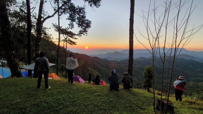 Sunrise Over Mountain Range at Pha Daeng National Park People seated and standing on a hilltop at sunrise with tents and mountain views at Pha Daeng National Park.