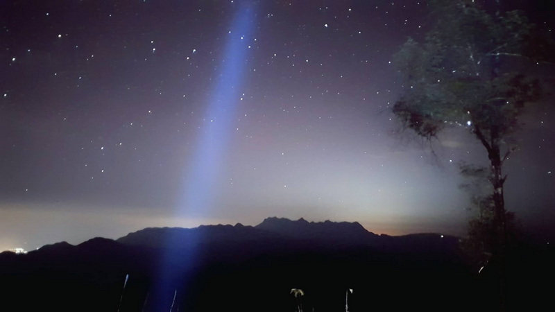 Starlit Night View with Light Beam at Pha Daeng National Park Night sky with stars, a bright light beam, and mountain silhouette at Pha Daeng National Park.