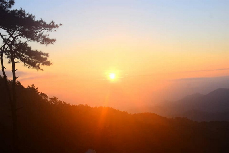 Sunset Over Mountain Range at Pha Daeng National Park Sunset scene with mountains, trees, and a bright orange sun in the sky at Pha Daeng National Park.