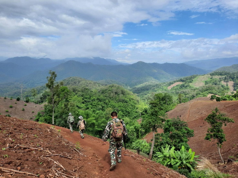 Soldiers walking on a dirt trail through lush green hills with mountains in the background at Pha Daeng National Park.