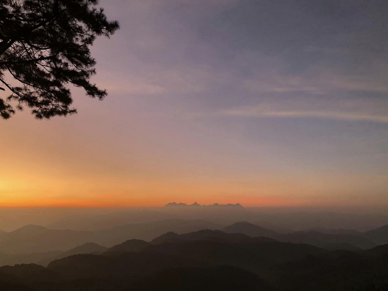 Sunset Over Mountain Ranges at Pha Daeng National Park Sunset over mountain peaks with colorful sky and silhouetted trees in the foreground at Pha Daeng National Park.