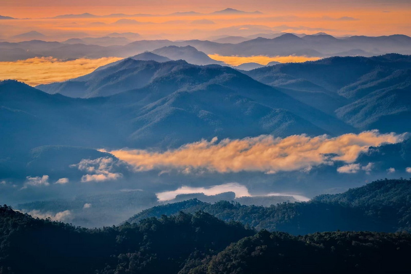 Scenic view of mountain ranges with clouds and warm sky lighting at Si Lanna National Park.