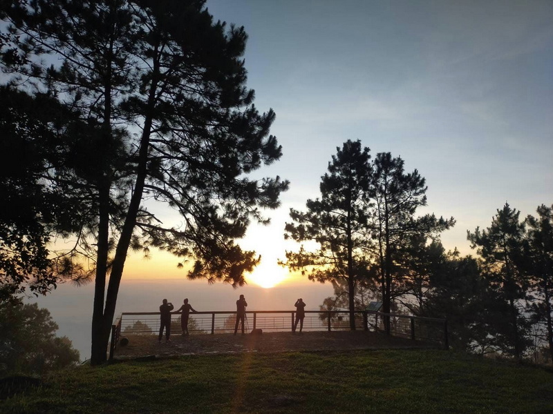 Sunset Viewpoint Over Misty Landscape at Si Lanna National Park Four silhouetted people stand on a platform watching a sunset through trees with misty scenery at Si Lanna National Park.