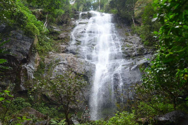 Tall waterfall flowing over rocks surrounded by dense forest greenery at Si Lanna National Park.