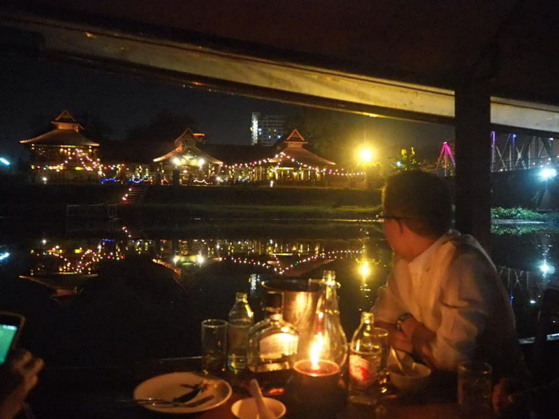 Person looking at city lights reflected on water from inside a boat at night at Chiang Mai Nightlife.