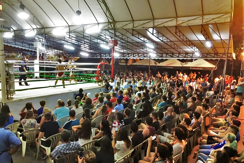 Nighttime Boxing Match at Night Tours In Chiang Mai Boxing match with fighters and spectators in an indoor arena at night at Night Tours In Chiang Mai.