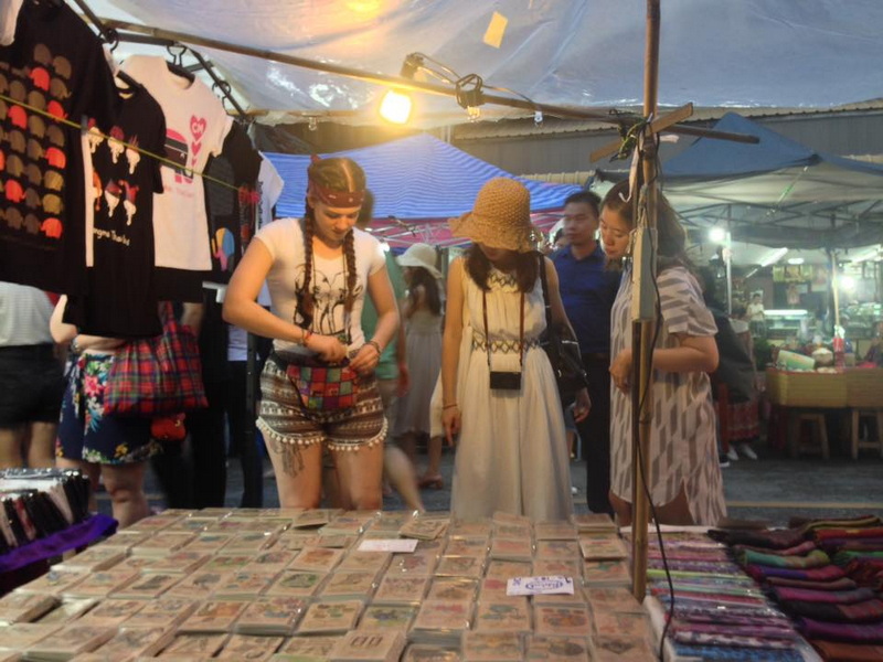 Night Market Shopping Scene at Things To Do In Chiang Mai Evening Women browsing market stall with clothing at night market scene at Things To Do In Chiang Mai Evening.