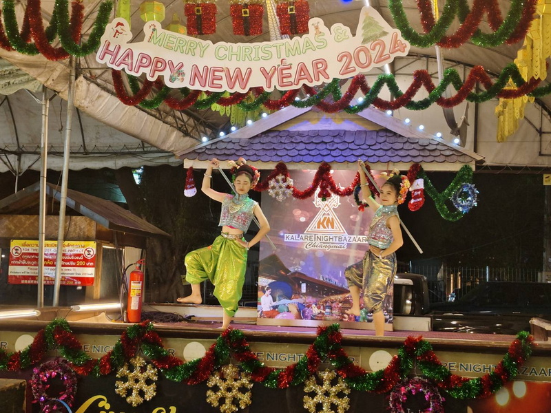 Two girls in colorful traditional Thai costumes dance on stage under Christmas decorations at night at Night Activities In Chiang Mai.
