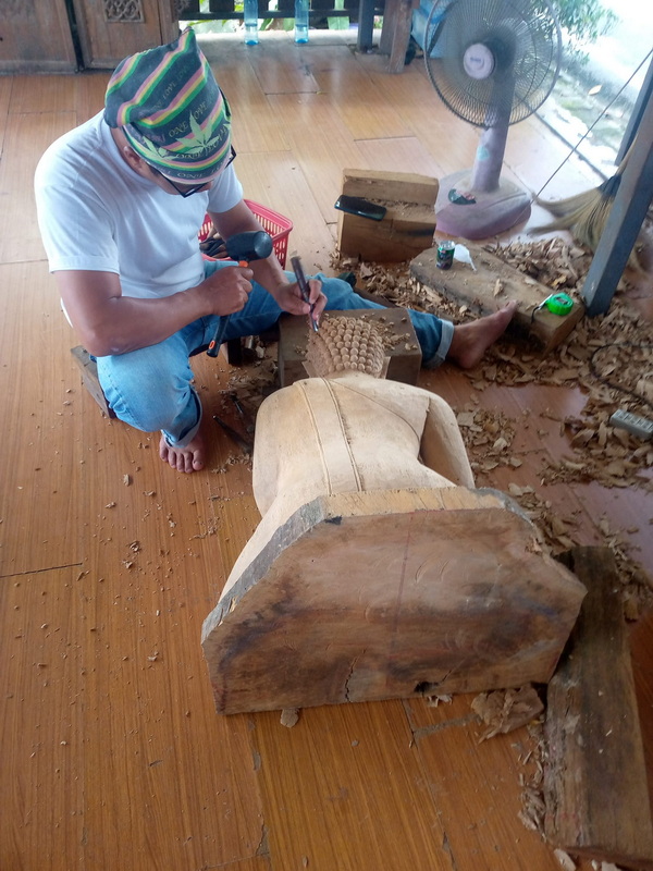 Wood Carving Workshop Scene at Baan Tawai Man carving wood with chisel and mallet inside a wooden workshop at Baan Tawai.