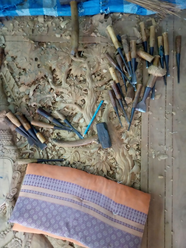 Carving tools and tools on a detailed carved wooden surface with cloth underneath at Baan Tawai Wood Carving Village.
