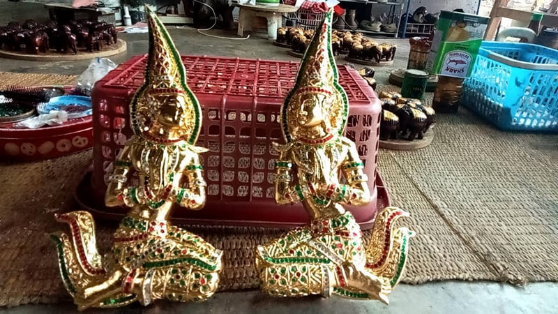 Two detailed gold mythological statues with tall pointed hats and ornate features at Baan Tawai Wood Carving Village.