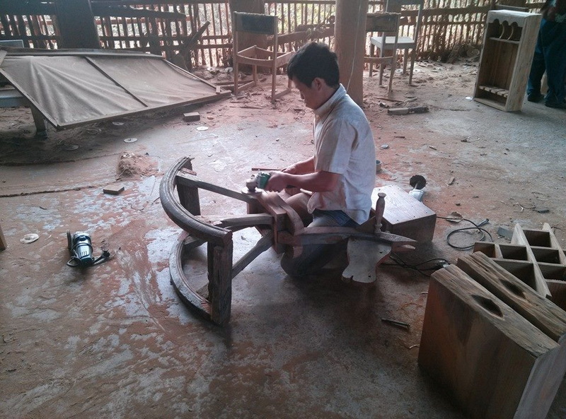 Person carving a wooden piece in a rustic workshop with woodworking tools around at Baan Tawai.
