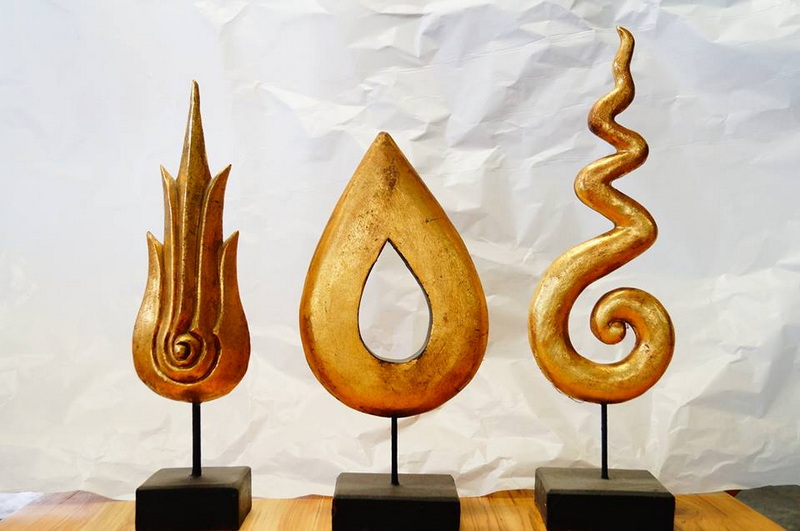 Three golden wooden sculptures on black pedestals against a white background at Baan Tawai.
