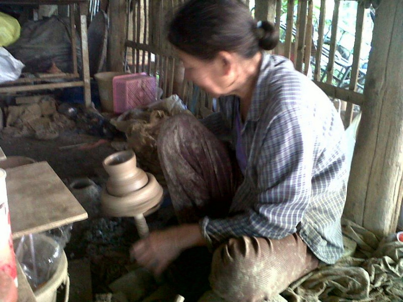 Traditional Pottery Craft at Baan Tawai Wood Carving Village Woman shaping a clay pot on a pottery wheel inside a wooden workshop at Baan Tawai Wood Carving Village.