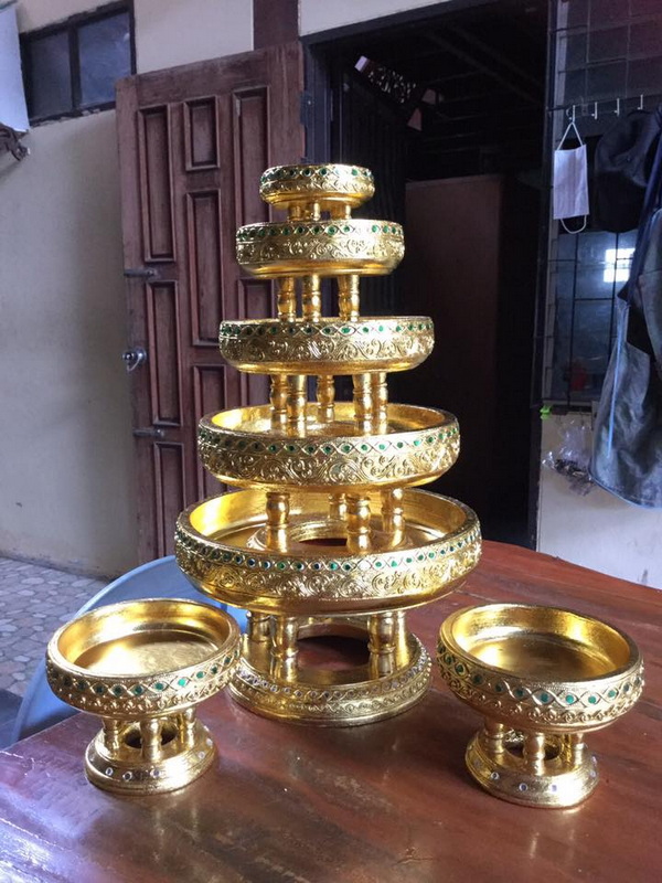 Golden multi-tiered decorative stand with intricate patterns on a wooden table indoors at Baan Tawai Wood Carving Village.