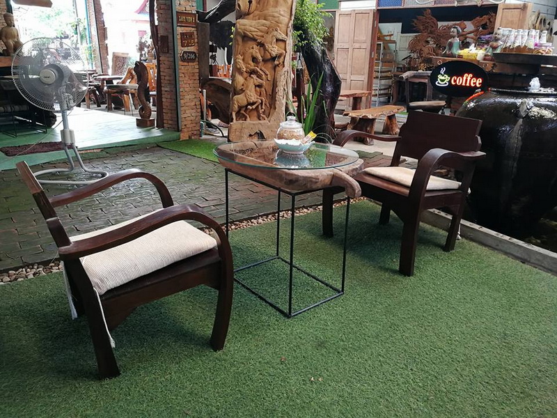 Two wooden chairs with cushions around a glass table on indoor artificial grass at Baan Tawai.