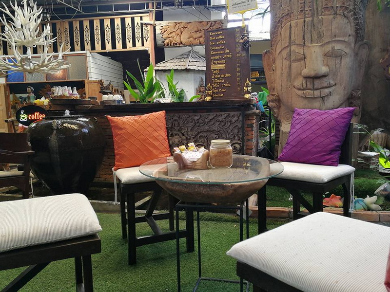 Outdoor Seating Area with Cushions at Baan Tawai Wood Carving Village Outdoor seating with colorful cushions and decorative art pieces surrounding greenery at Baan Tawai Wood Carving Village.