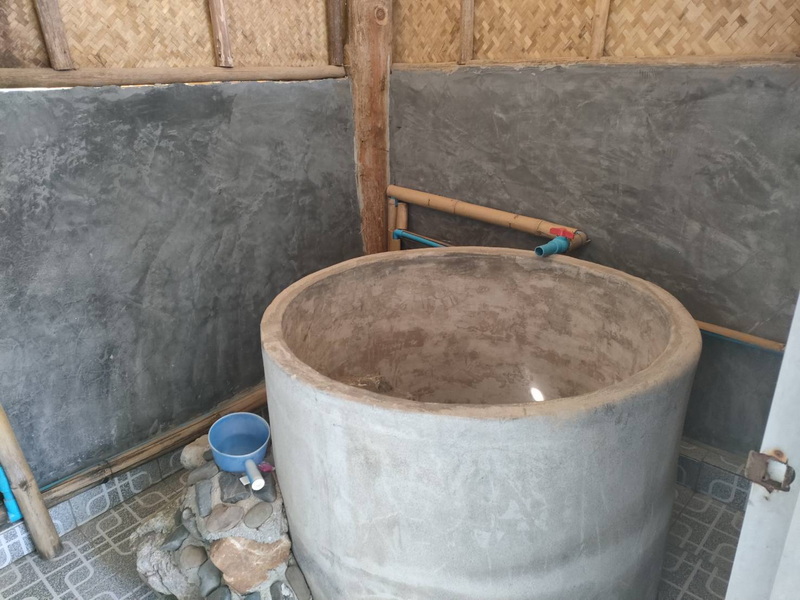 Indoor Concrete Bath with Pipes at Ban Yang Pu Toh mineral hotsprings Indoor concrete bath with blue pipe and unfinished walls, small rocks nearby at Ban Yang Pu Toh mineral hotsprings.