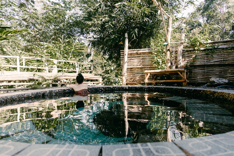 Serene Outdoor Hot Spring at Ban Yang Pu Toh Person relaxing in a circular outdoor hot spring with trees and wooden fencing around at Ban Yang Pu Toh.