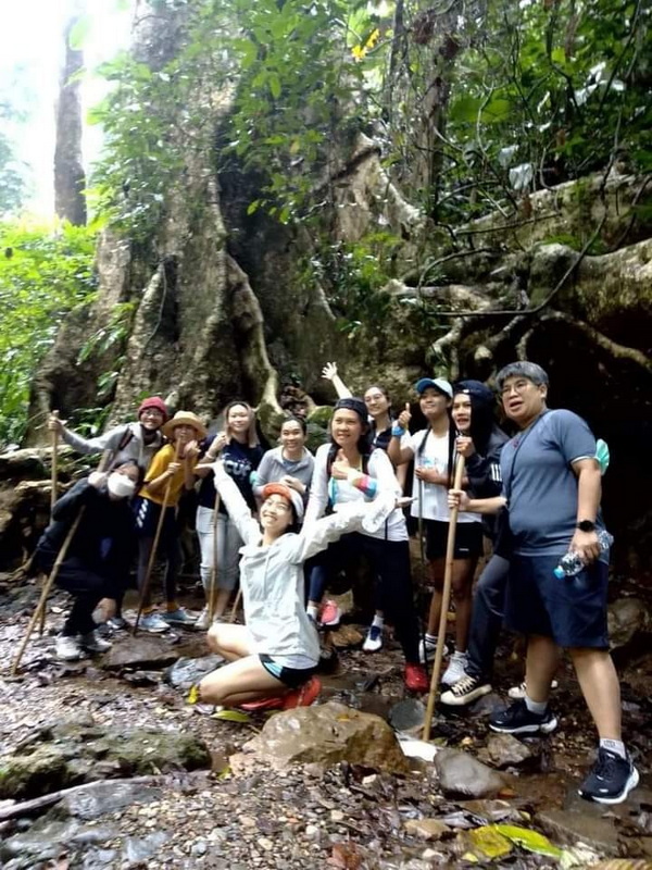 Group of hikers posing on a rocky forest trail surrounded by large trees at Ban Yang Pu Toh.