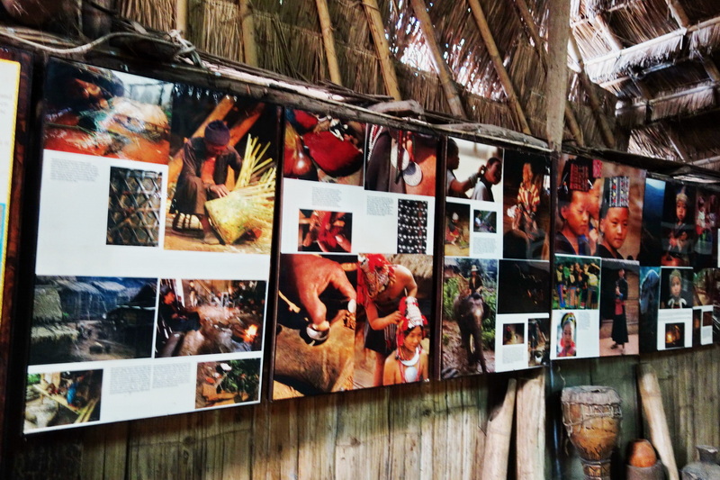 Indoor display with posters showing traditional activities and portraits inside a bamboo shelter at Doi Pui Hmong Village.